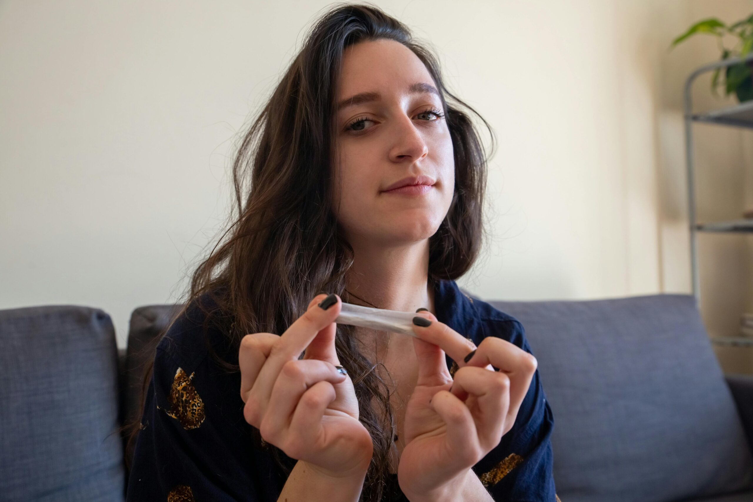 Young woman holding smoking paper, sitting on a sofa, enjoying a moment of relaxation indoors.